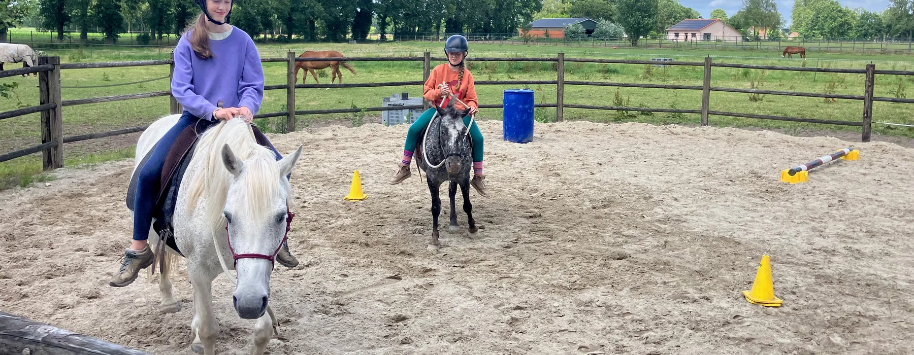 Kinderen rijden samen met hun pony's in de buitenpiste